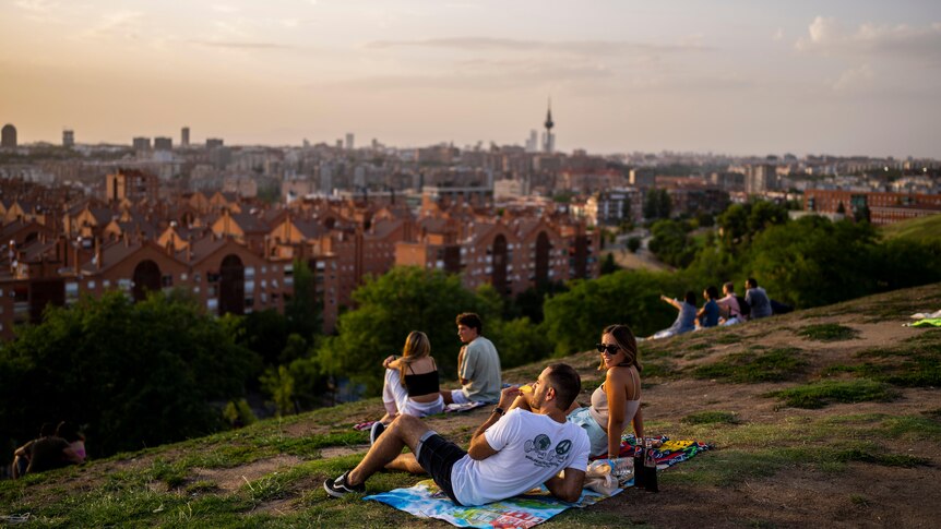 A group人们在俯瞰马德里的绿色山顶上的野餐垫上休息